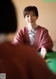 A woman in a red kimono sitting at a green table.