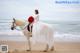 A woman in a white dress riding a white horse on the beach.