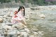 A woman in a pink kimono sitting on a rocky beach.