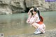 A woman in a pink kimono sitting on the shore of a lake.