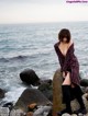 A woman sitting on a rock by the ocean.