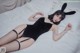 A woman laying on a bed wearing a black bodysuit and bunny ears.